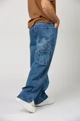 Jean de corte baggy con diseño carpintero, confeccionado en denim azul clásico. Presenta un ajuste holgado, tiro medio y bolsillos laterales utilitarios característicos del estilo carpintero.