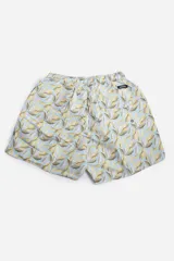 Short de baño celeste con estampado de hojas pequeñas en tonos verdes y blancos. Cuenta con cintura elástica con cordón ajustable, bolsillos laterales y un parche circular con logo en la parte inferior.