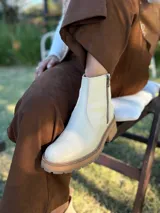 Bota corta de cuero vacuno con textura granulada, color crudo. Presenta cierre lateral metálico, tirador en la parte trasera y suela track de goma en tono contrastante.