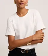 Blusa blanca de poliéster con cuello redondo, mangas cortas, cierre trasero en forma de gota, pequeñas aberturas laterales y acabados en pespuntes en las mangas y el cuello.