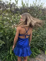 Vestido corto color bordó con escote en V, diseño de top triangular y aberturas laterales en la cintura. Presenta breteles finos cruzados en la espalda y falda con doble volado irregular en el ruedo.
