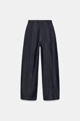 Jeans de tiro alto con corte balloon y largo completo. Presentan cintura con trabillas, bolsillos laterales ocultos, pinzas en el delantero y pespuntes marcados a contraste. Cierre frontal con cremallera, botón y ganchos metálicos.