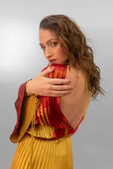 Vestido largo plisado con estampado abstracto en tonos rojo, naranja y dorado, cuello alto y mangas acampanadas. Incluye lazo fino para ajustar en la cintura.