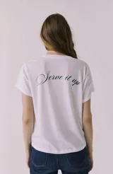 Remera blanca de manga corta y cuello redondo, con un estampado pequeño en el pecho que dice "Apres Tennis" en tonos verde lima y rosa.