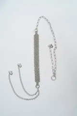 Cinturón de cadena plateada con diseño de malla central de esferas pequeñas y terminaciones con dijes en forma de corazón.