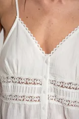 Top blanco de algodón peinado con tirantes finos, escote en V con detalle de encaje y cierre frontal abotonado. Presenta inserciones de encaje transparente en el abdomen y un diseño fluido en la parte inferior.
