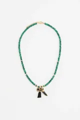 Collar de cuentas de vidrio facetadas en color verde con detalles dorados, que presenta un conjunto de dijes colgantes que incluyen una borla negra, un dije con piedra negra y un dije en forma de colmillo.