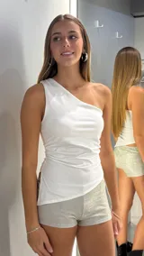 Top de un solo hombro color blanco, con diseño ajustado y detalle de frunces laterales.