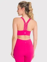 Top deportivo de color fucsia con diseño de espalda nadadora con tirantes decorativos de encaje. Cuenta con sujetador integrado y almohadillas removibles, ofreciendo soporte medio.