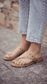 Sandalias chatas de cuero color bordó, con diseño de tira ancha que envuelve el empeine y sujeta el dedo gordo, decoradas con tachas metálicas doradas.