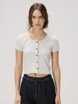 Remera corta de corte ajustado, color gris melange, con cuello redondo y cierre frontal de botones tipo cardigán.