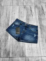 Short de jean tiro bajo color azul, con detalles de roturas y efecto desgastado.