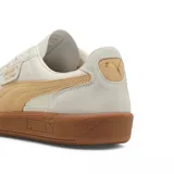 Championes Puma modelo Palermo LTH, con diseño de perfil bajo, cuerpo de cuero blanco, detalles en gamuza gris y franja lateral en color lila. Cuenta con suela de goma color caramelo y logo dorado en el lateral.