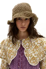 Camisa de popelina de algodón color mostaza con estampado floral blanco. Presenta un cuello amplio con terminación ondulada y encaje de algodón crudo, mangas largas y botones de nácar en el frente.