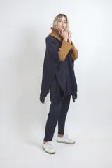 Poncho tejido de punto grueso color azul marino con cuello alto ocre y flecos en el ruedo.