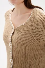 Cardigan de punto color natural, con cuello en V, cierre frontal con botones y diseño holgado. Presenta detalles de costuras decorativas bordadas a lo largo de las mangas y en los bordes.