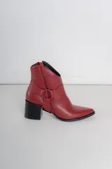 Bota corta de cuero color bordó, con taco cuadrado y punta fina. Presenta una correa con tachas pequeñas y una argolla metálica decorativa alrededor del tobillo. Cuenta con cierre lateral.