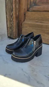 Zapatos de tacón alto y plataforma con diseño de caña baja, confeccionados en combinación de cuero liso, charol y detalles con textura animal print. Presentan cierre lateral de cremallera y suela gruesa con costuras visibles.