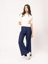 Pantalón de lino color beige, de tiro alto, pierna ancha y levemente acampanada. Tiene pinzas delanteras, elástico en la pretina trasera, cierre delantero y broche interno, bolsillos laterales y dobladillo invisible.