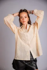 Camisa blanca de broderie, con cuello clásico, cierre frontal con botones, mangas largas abullonadas y puños con botón.
