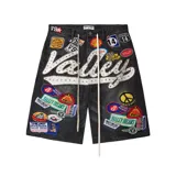 Short de jean negro con corte baggy, decorado con múltiples parches bordados coloridos y una gran inscripción frontal con apliques de pedrería. Incluye cordones largos en la cintura.