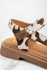 Sandalias con estampado animal print de vaca, con suela marrón y hebilla ajustable.