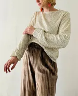 Blusa de lentejuelas color crema, de mangas largas con puños elásticos.