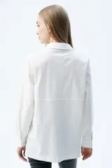 Camisa de corte recto con cuello clásico y cierre frontal de botones. Presenta un parche bordado con mostacillas en tonos blanco y negro en el frente, con diseño de estrellas y formas abstractas.