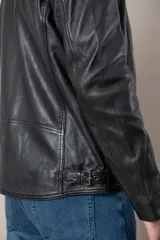 Campera de cuero negro con capucha gris desmontable, cierre frontal, bolsillos con cierre y detalles de hebillas en el cuello y la cintura.