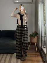 Pantalón tipo palazo de corte amplio y tiro alto, confeccionado en tela con estampado de cuadros escoceses en tonos marrones, blancos y negros. Cuenta con cintura elástica y bolsillos laterales.