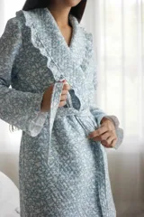 Bata larga celeste con estampado de pajaritos blancos, confeccionada en algodón capitoneado con volados en la solapa y puños. Incluye lazo de algodón capitoneado para ajustar en la cintura.