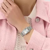 Reloj analógico Guess modelo Bonnet con caja rectangular de acero inoxidable plateado y esfera blanca con números romanos. Presenta un diseño con cristales engastados en los laterales de la caja y malla de acero tipo milanesa.