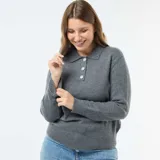 Sweater de punto gris con cuello polo, manga larga y puños acanalados. Presenta una abertura frontal con tres botones decorativos tipo joya con brillos.