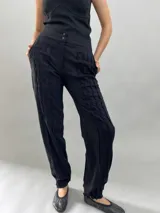 Pantalón tipo babucha confeccionado en lana de oveja, color visón. Presenta un diseño de tiro alto con textura vertical plisada a lo largo de las piernas, cintura con cierre de doble broche y puños elásticos en los tobillos.