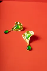 Aro colgante dorado con forma de hoja ondulada, con una piedra central verde claro y una lágrima de jade verde oscuro colgando.