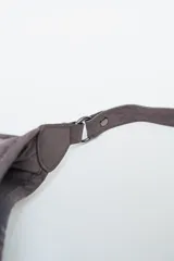 Cartera tipo hobo color gris oscuro, con flecos largos en la parte inferior y detalles de tachas plateadas. Tiene una correa ajustable para el hombro.