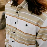 Camisa de franela a rayas horizontales en tonos beige, marrón y blanco, con cuello clásico, cierre frontal con botones y dos bolsillos con solapa en el pecho.
