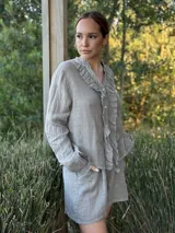 Camisa de lino color gris claro, de manga larga y corte holgado, con cuello mao y detalle de volados en el frente a lo largo de la botonera.