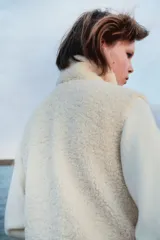 Chaleco de tejido sherpa color crema, con cuello alto, cierre frontal y bolsillos parche delanteros.