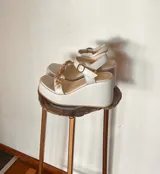 Sandalias de plataforma blanca con taco chino, tira en el empeine decorada con piedras acrílicas translúcidas y tira ajustable al tobillo con hebilla dorada.