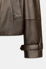 Cazadora de Zara Woman Collection confeccionada en material efecto piel color marrón oscuro. Presenta cuello con solapas, cierre frontal cruzado con botones, bolsillos delanteros y mangas largas con trabillas y hebillas ajustables en los puños.