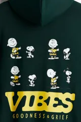 Canguro verde oscuro de peso medio con interior cepillado suave. Tiene bolsillo canguro, capucha de doble capa con cordón de ajuste y frente cruzado. Puños y bajo acanalados. Corte estándar. Estampado frontal con la palabra "VIBES" en amarillo.