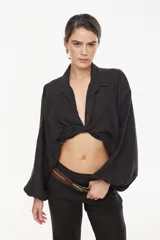 Top corto de lino italiano con diseño a cuadros en tonos verde oliva, beige y rosado, cuello camisero, mangas largas abullonadas con puños elásticos y nudo frontal ajustable.