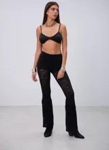 Pantalon de encaje negro con corte ajustado en la parte superior y botamanga acampanada, con diseño de encaje floral semitransparente.