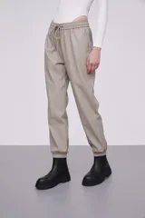 Pantalón tipo babucha de eco cuero color cemento, con cintura elástica y cordón de ajuste, bolsillos laterales y puños elásticos en los tobillos.