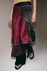 Pareo tipo pañuelo con diseño cruzado y cierre de lazada en la cintura. Presenta una combinación de paneles en color bordó con estampado de lunares y un panel lateral en color verde oscuro con microestampado, ambos con bordes definidos.
