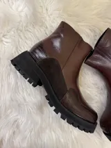 Bota corta de cuero color chocolate con suela track negra. Presenta una combinación de texturas que incluye cuero liso, gamuza y detalles con textura de reptil en la puntera y el talón.