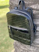 Mochila de cuero sintético color negro con diseño combinado: parte superior con textura de reptil y parte inferior con diseño acolchado capitoneado. Cuenta con bolsillo frontal con cierre metálico y tirador decorativo.
