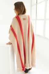 Ruana artesanal de tejido de punto, color beige con franjas horizontales gruesas rojas y finas amarillas. Posee flecos en el borde inferior.