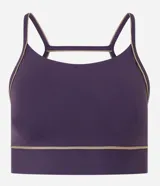 Top deportivo de microfibra en color violeta con detalles de friso en tono arena. Presenta un diseño de escote redondo, breteles finos y una banda inferior elástica que proporciona mayor sujeción. Incluye copas removibles para mayor comodidad.